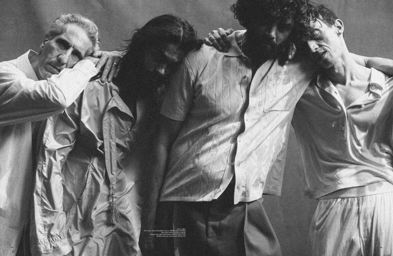 Monochrome portrait of four men closely standing with arms around each other, wearing dress shirts in a studio setting.
