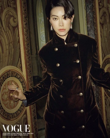 Elegant woman in a double-breasted brown velvet coat opening an ornate gold door in an opulent interior with soft, diffused lighting.