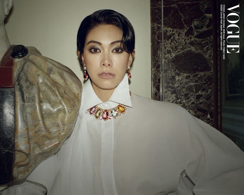 A woman with short, dark hair wearing a white collared shirt and colorful necklace posing next to a stone horse sculpture inside.