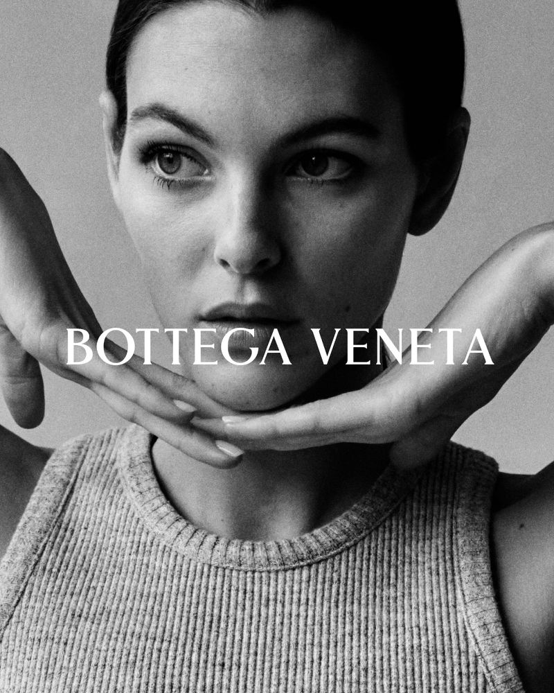 Black and white portrait of a model with hands framing her face wearing a gray ribbed tank top, featuring the Bottega Veneta logo.