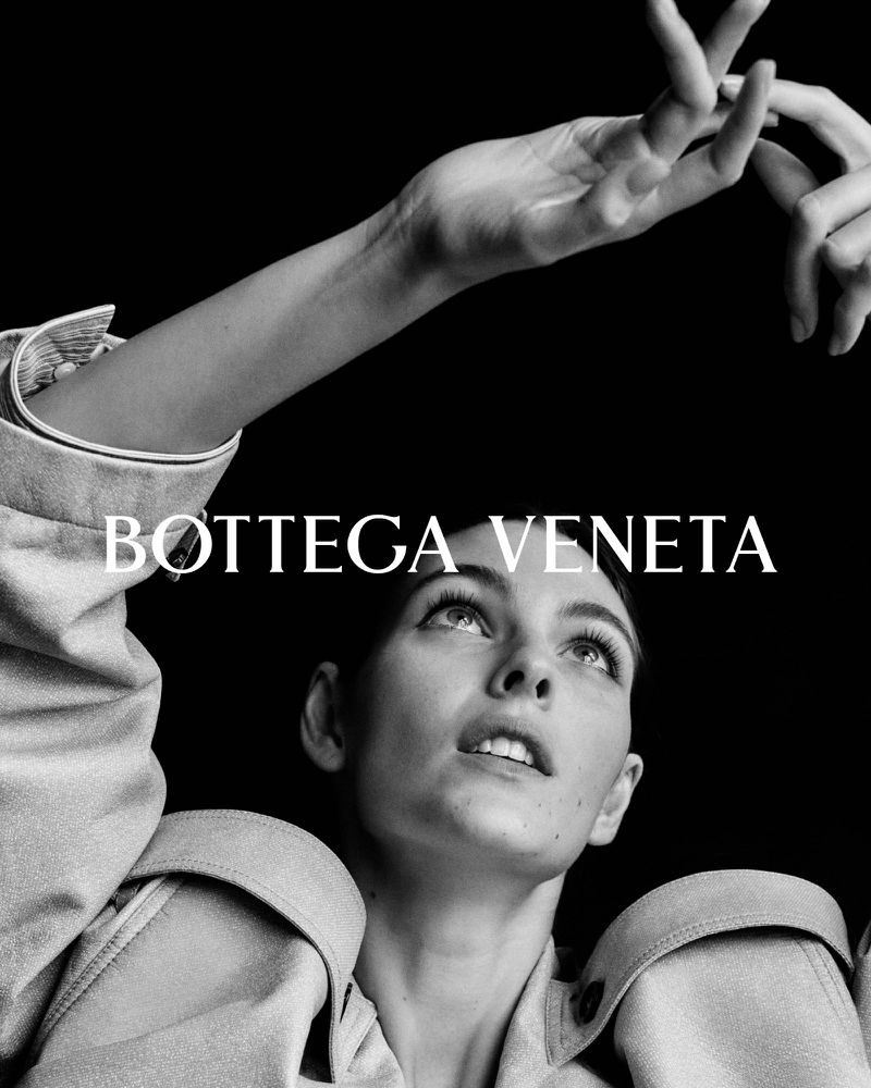 Black and white fashion advertisement featuring a woman in a jacket looking upwards, with the brand name Bottega Veneta visible.