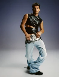Musician Edis poses wearing a black sleeveless cutout top and silver foil accented light-wash wide-leg denim jeans in a studio setting.