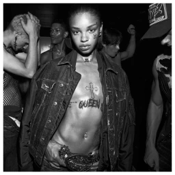 Black and white portrait of a model in a denim jacket surrounded by a group of people in a dark venue