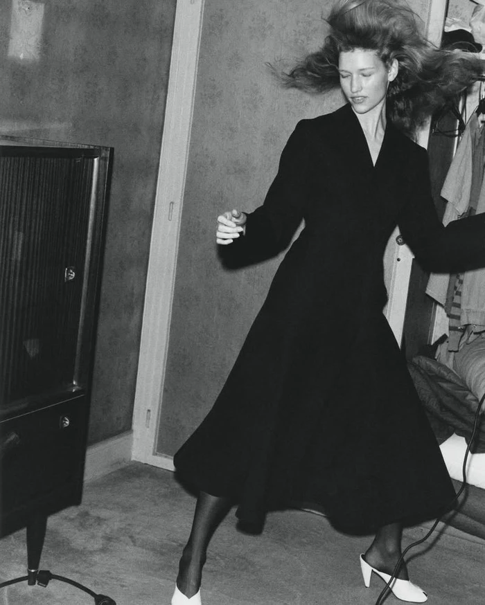 Model Apolline Rocco Fohrer in a long black coat tossing her hair in an editorial photograph for D Repubblica.