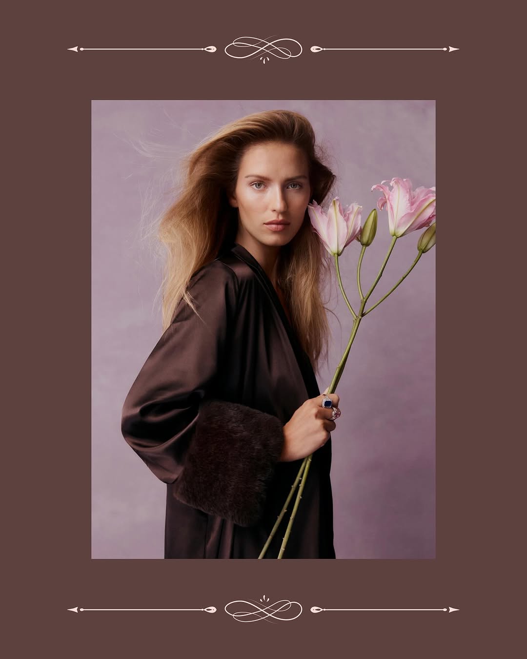 Portrait of a blonde woman in a brown robe holding pink lilies against a muted purple background with a dark brown ornamental border.