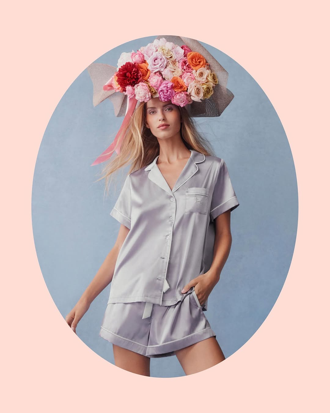 Woman in silk pajama set with floral headpiece poses in a studio against a blue backdrop, in fashion beauty style.