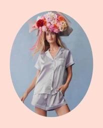 Model wearing silver satin pyjamas and a large floral hat against a blue backdrop for Peter Alexander