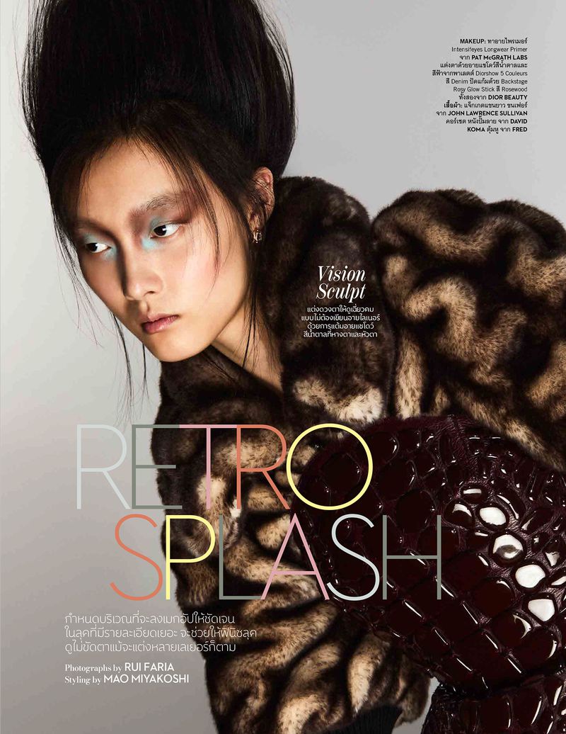 Editorial fashion shot featuring a young Asian model with creative makeup and fur coat posing in a photo studio with grey background.