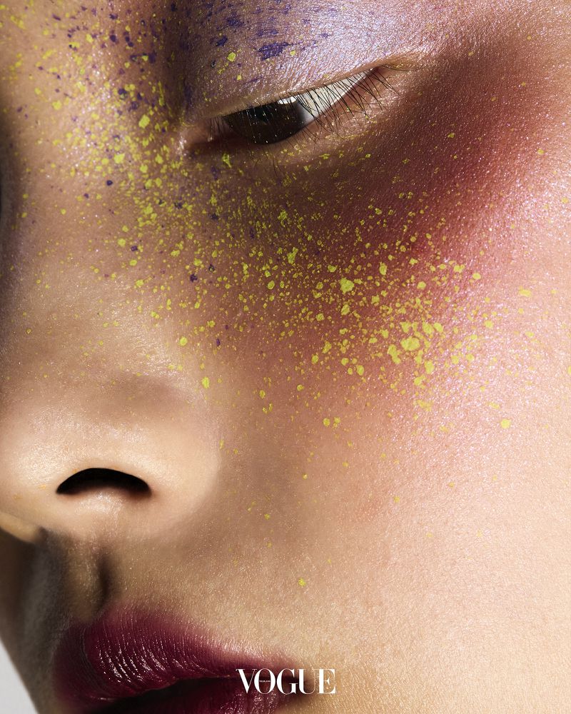Close-up of a woman's face featuring artistic yellow and purple makeup, creating a vivid and textured beauty image, skin detail.