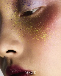 Extreme close-up beauty portrait showing an eye with purple shadow, yellow speckles across the cheek, and deep plum lipstick.