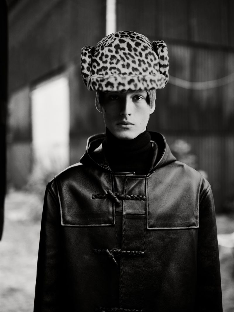Monochrome portrait of a person wearing a leopard print hat and hooded jacket, standing in front of a blurred background.