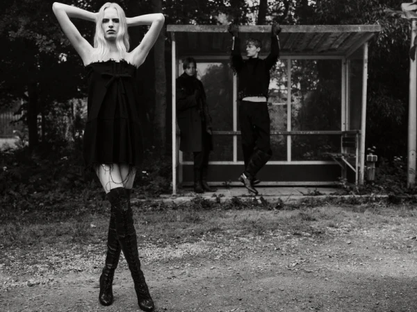 Marrit Krikke in a black strapless dress and thigh-high boots posing outdoors in front of a bus stop shelter with two male models.