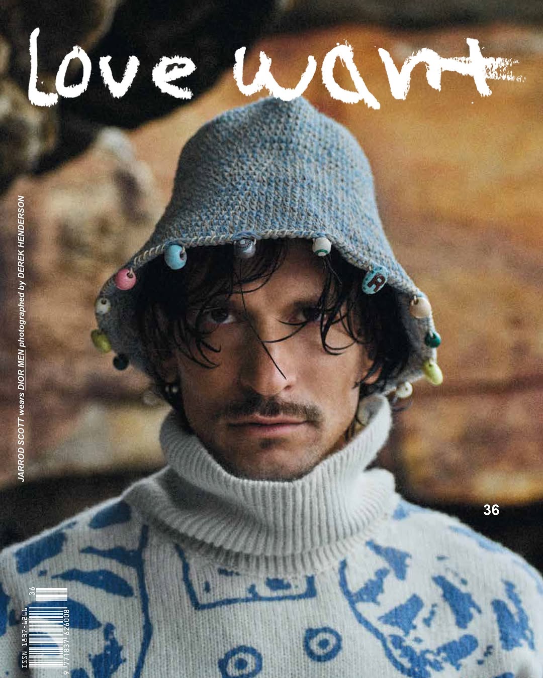 Close-up fashion shot featuring a male model with a beaded bucket hat and patterned turtleneck, showcasing editorial style and fashion industry appeal.