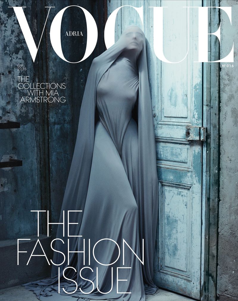 Vogue magazine cover featuring a figure draped in gray fabric standing against a weathered blue door, evoking a muted, artistic aesthetic.