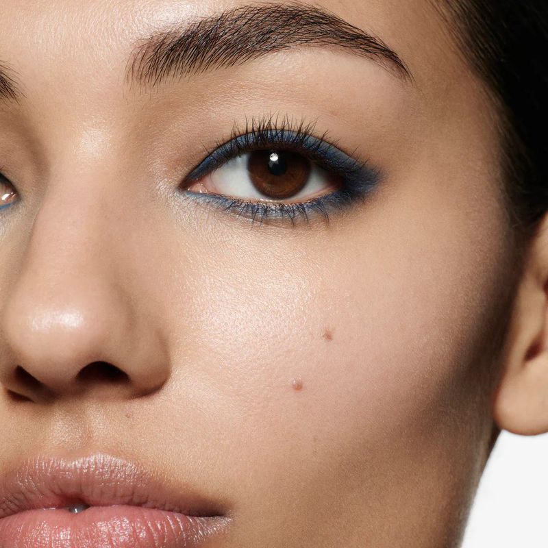 Close-up of a woman's face shows detailed makeup with blue eyeliner, defined eyelashes, and clear skin. Focus on beauty and cosmetics.