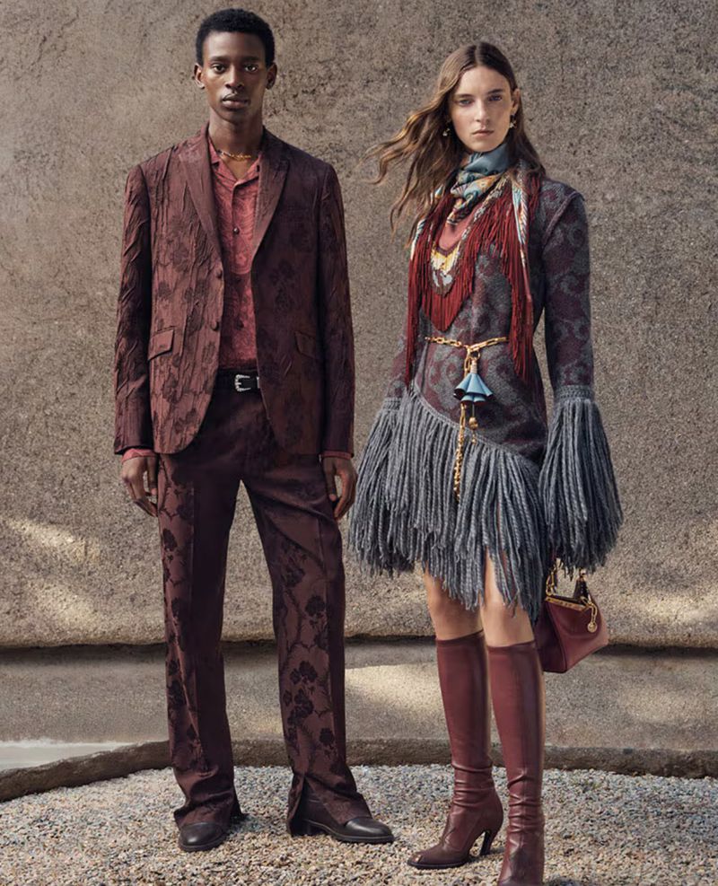 Fashion editorial shot of a Black male model in a brown patterned suit and a White female model in a grey dress with fringe.