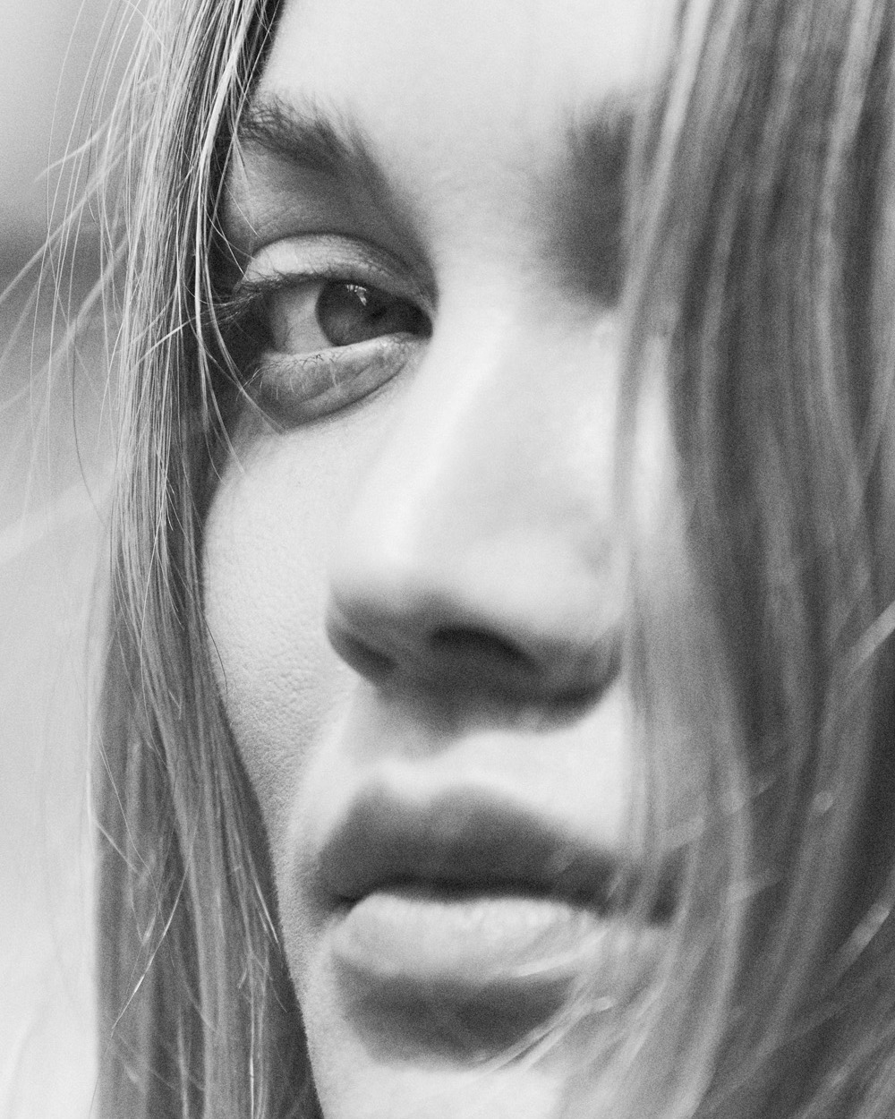 Extreme close-up monochrome portrait of a woman with loose hair falling across her face for Love Want magazine