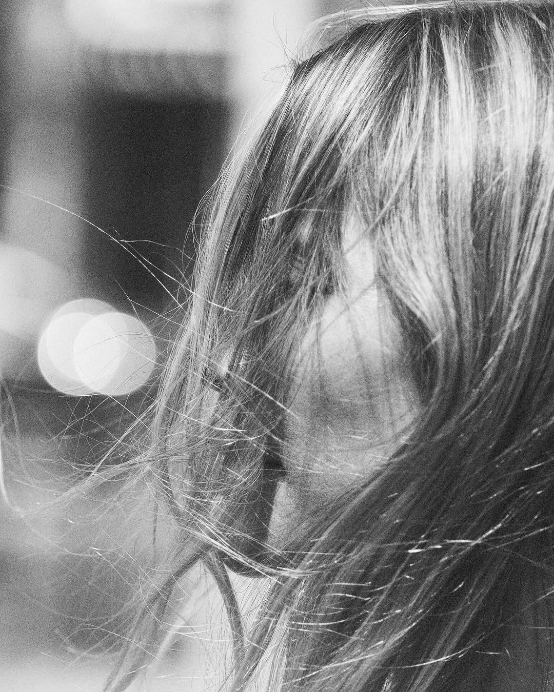 Close-up portrait of a woman with long hair blowing across her face in black and white.