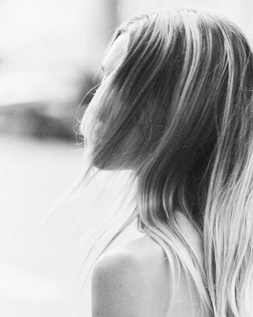 Close-up portrait of a woman in profile with long blonde hair blowing across her face for a Love Want editorial by Bart Celestino.