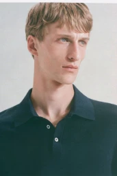 Portrait of a young white male model wearing a dark navy blue polo shirt against a plain light background.