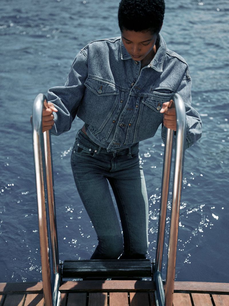 Model Laiza de Moura climbing a boat ladder over open water wearing a denim jacket and matching jeans.