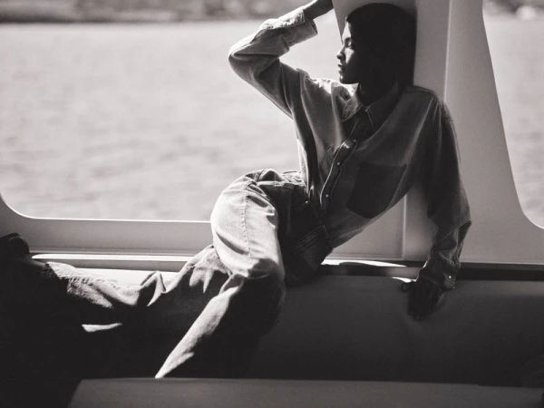 Laiza de Moura reclines in a denim shirt and jeans next to a sunlit boat window in black and white.