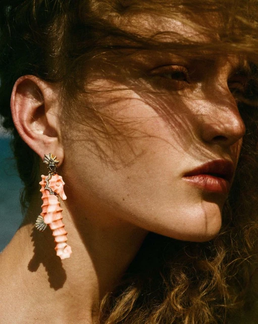 Close-up of a fair-skinned adult female wearing a large seahorse earring, with dramatic shadows falling across her face and hair.