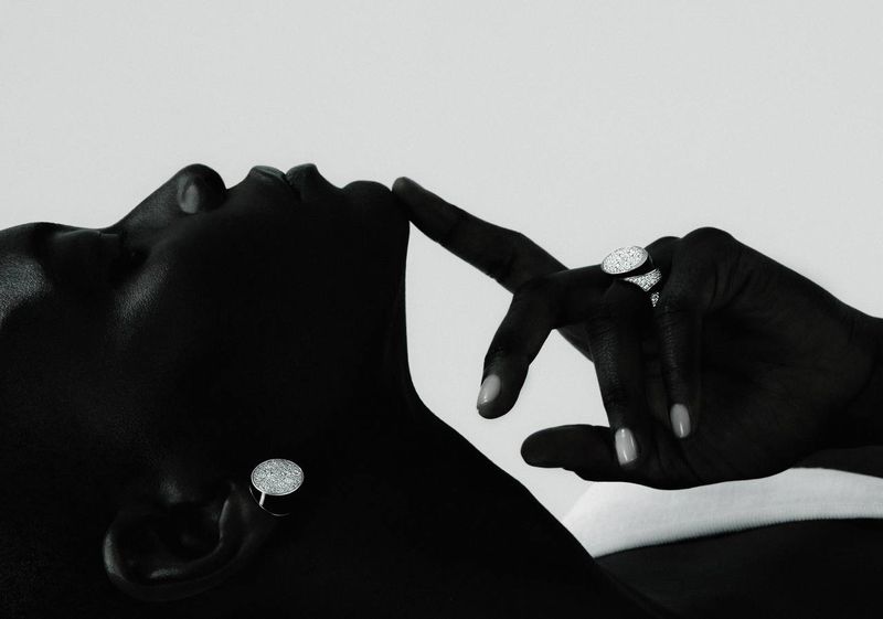 Close-up of a Black adult woman's face and hand with sparkling jewelry, lying against a light background in a studio setting.