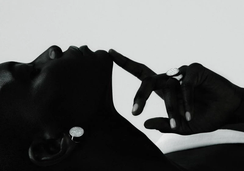 Close-up of a Black adult woman's face and hand with sparkling jewelry, lying against a light background in a studio setting.