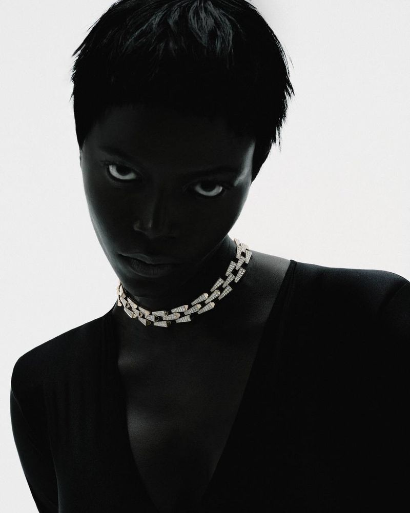 High-contrast portrait of a Black woman with short hair wearing a diamond chain choker necklace against a bright white background.