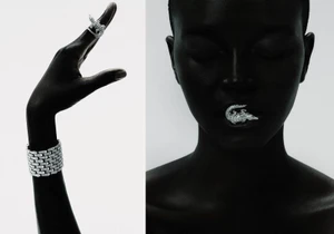 Black woman posing with diamond crocodile jewelry in her mouth alongside a raised hand with matching ring and cuff on white background.