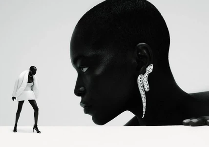 Black and white fashion shot of a Black woman's profile wearing a diamond serpent earring next to a miniature figure in a white mini dress.