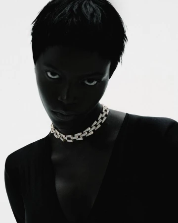 High-contrast portrait of a Black woman with short hair wearing a diamond chain choker necklace against a bright white background.