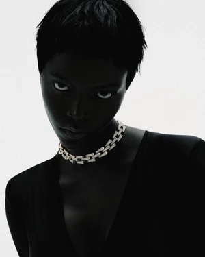 High-contrast portrait of a Black woman with short hair wearing a diamond chain choker necklace against a bright white background.
