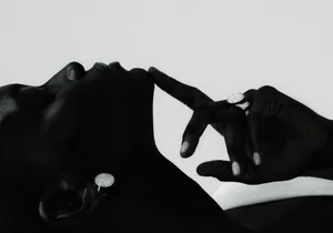 Close-up black and white profile of a Black model touching their chin while wearing a round pavé diamond earring and matching ring.