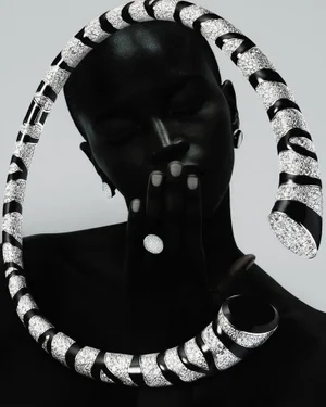 Model wearing diamond jewellery and a large curved patterned neckpiece in a high-contrast black and white studio portrait.