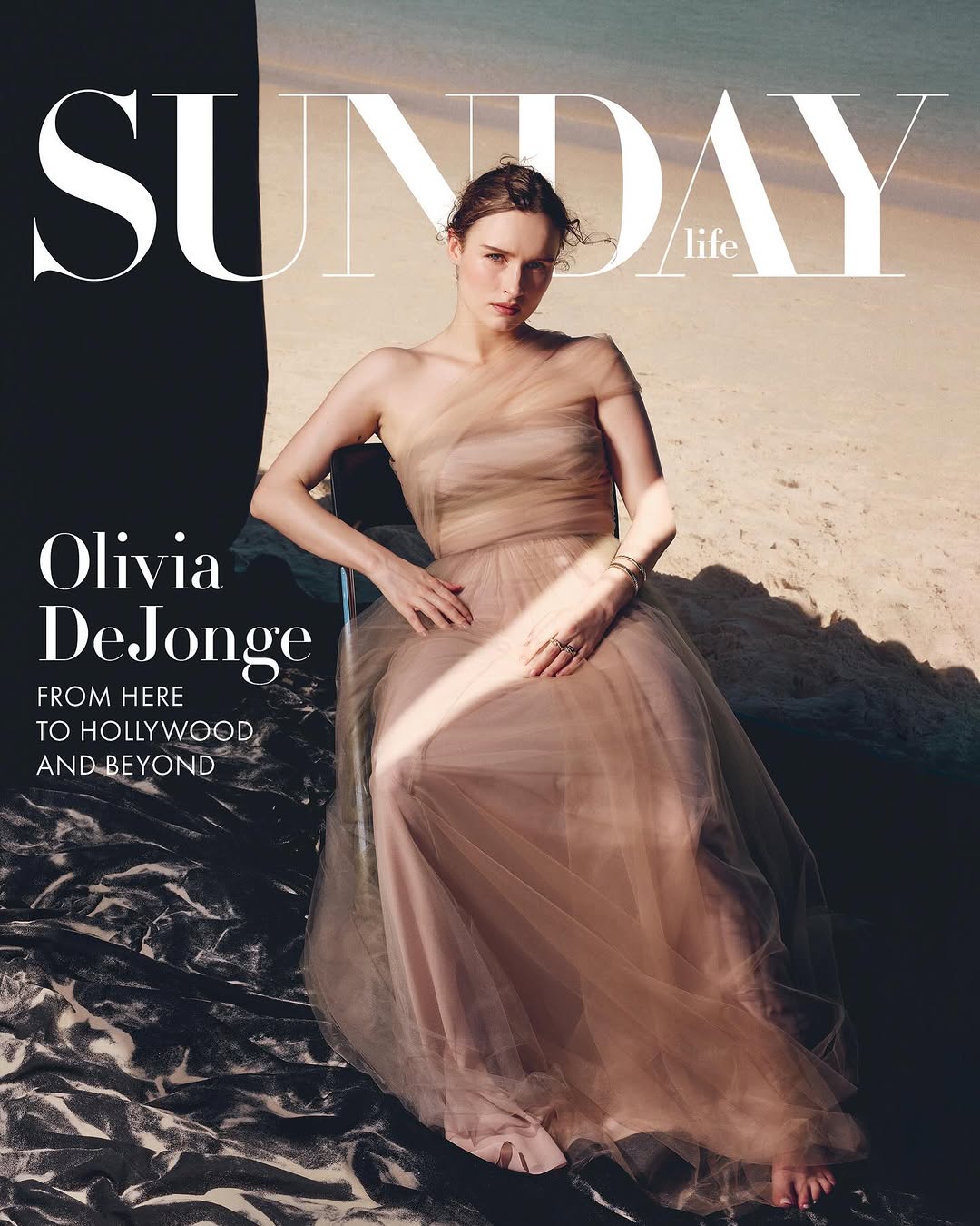 Olivia DeJonge poses on Sunday Life cover in flowing gown. The beach scene backdrop and gown are muted tones, soft, and feminine.