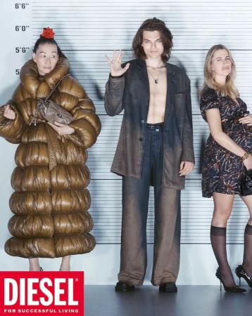 Three models stand in a lineup against a height chart in a studio. The woman on the left wears a large puffer coat, the man is shirtless, and the woman on the right wears a dress.