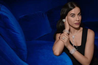 Woman wearing diamond jewelry and a black top seated against a deep blue velvet sofa for Vogue Mexico