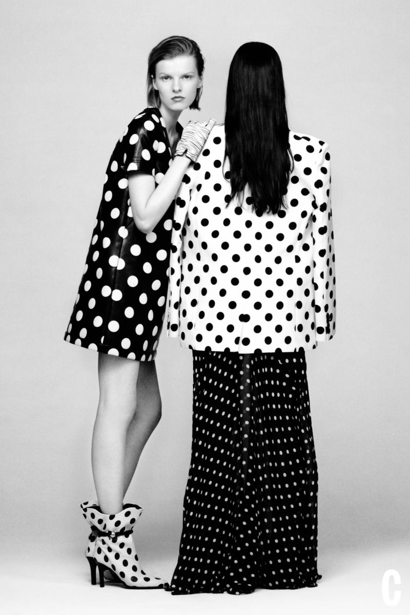Two fashion models wear polka dot clothing in a studio. One model stands facing forward in a maxi skirt, the other wears a dress.