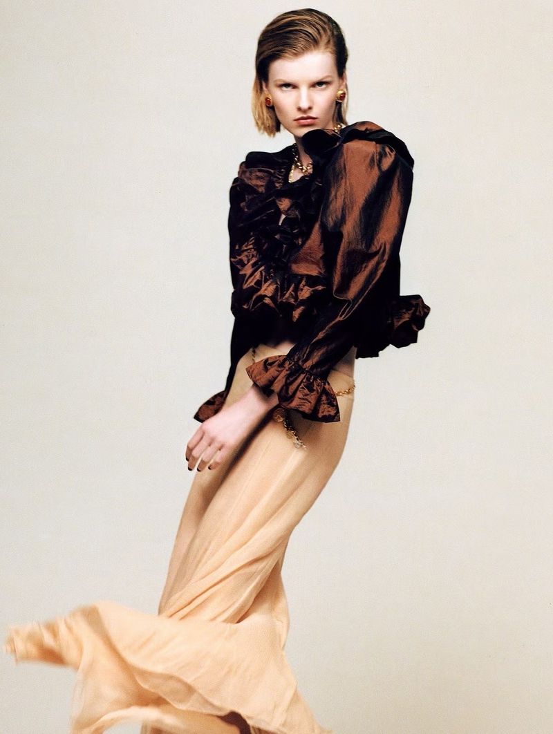 Model Lexy Hearn posing in a brown ruffled blouse and flowing beige maxi skirt against an off-white studio background.
