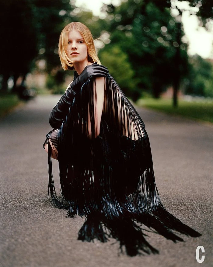 Model in black fringe dress and leather gloves squatting on a park path for Cosmopolitan U.S. Fall Fashion editorial by Arturo Alcala