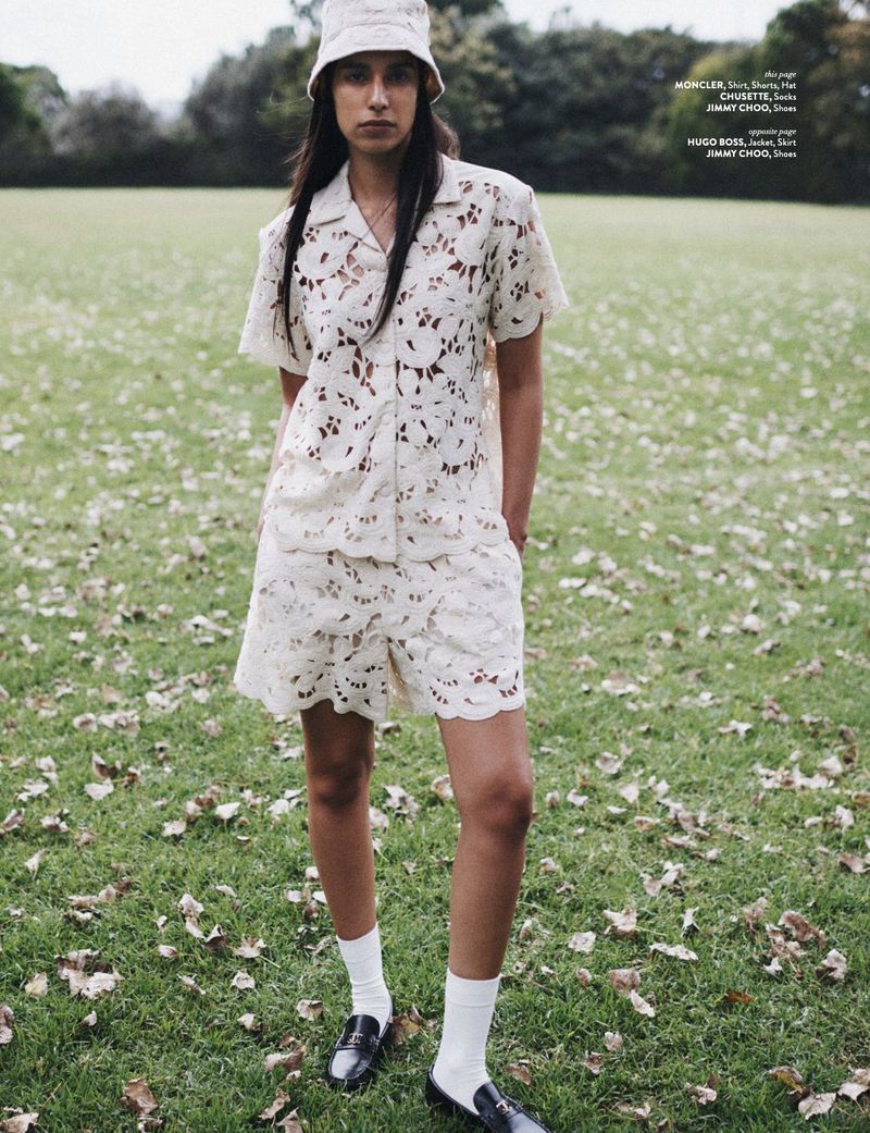Woman in a matching eyelet bucket hat, shirt, and shorts stands in a grassy field with fallen leaves wearing socks and loafers.