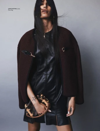 Fashion editorial shot of a woman with dark hair wearing a leather dress and jacket, holding a Louis Vuitton handbag in a studio.