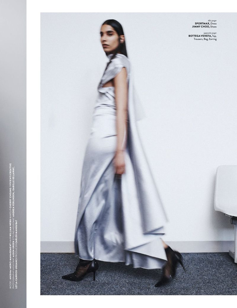 Editorial fashion shot: a woman in a silver dress and high heels walks against a white wall in a photo studio. The photo is blurred.
