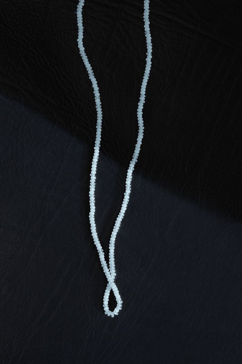 Close-up of a light blue beaded necklace draped over a black leather surface with visible grain texture and a soft lighting gradient.