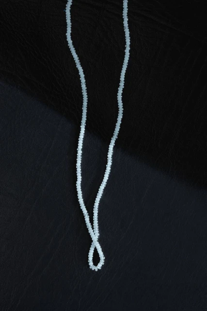 Close-up of a light blue beaded necklace draped over a black leather surface with visible grain texture and a soft lighting gradient.