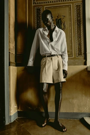 Adult male fashion model in casual wear poses in an ornate corner with architectural trim, neutral colors, and soft, diffused lighting.