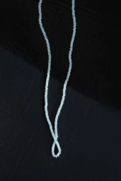 A delicate strand of pale beads forming a loop and swinging against a dark textured background.