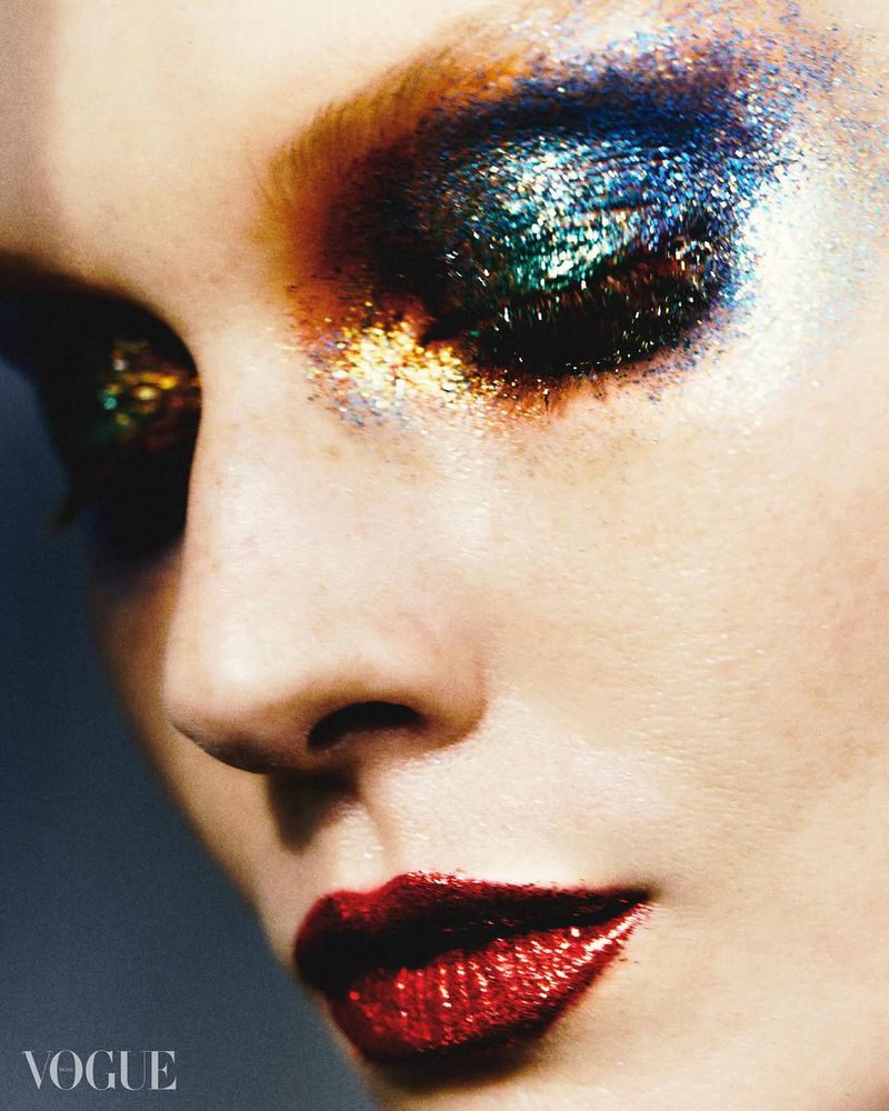 Close-up studio shot of a fair-skinned adult female model with heavy glitter eye makeup and glossy red lips. Beauty and fashion concept.